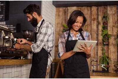 Une serveuse qui regarde sa tablette et un homme qui prépare du café